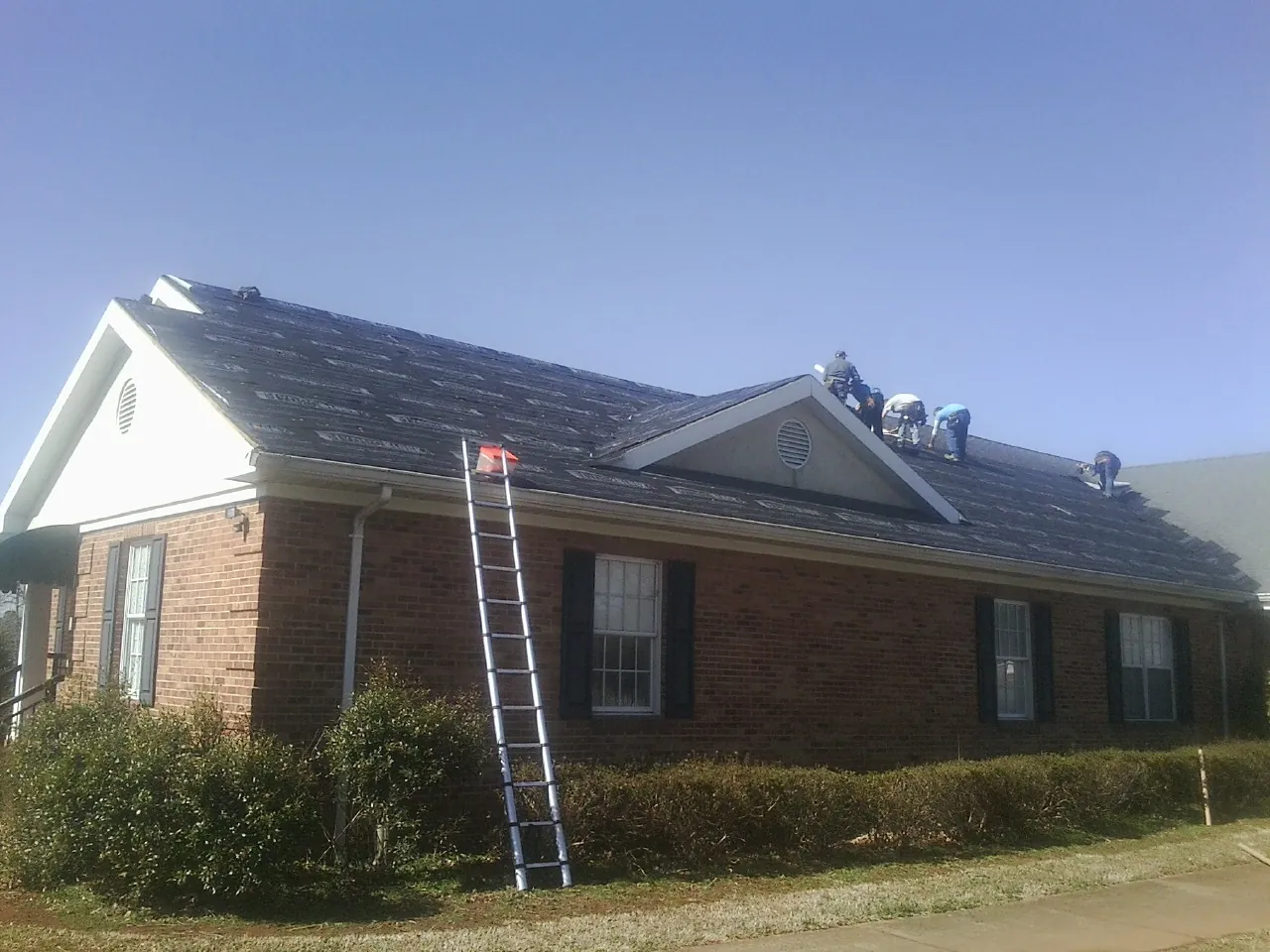 Crew tearing shingles off a brick ranch roof with a ladder set — Emergency Roof Repair work by our crew in Rossville