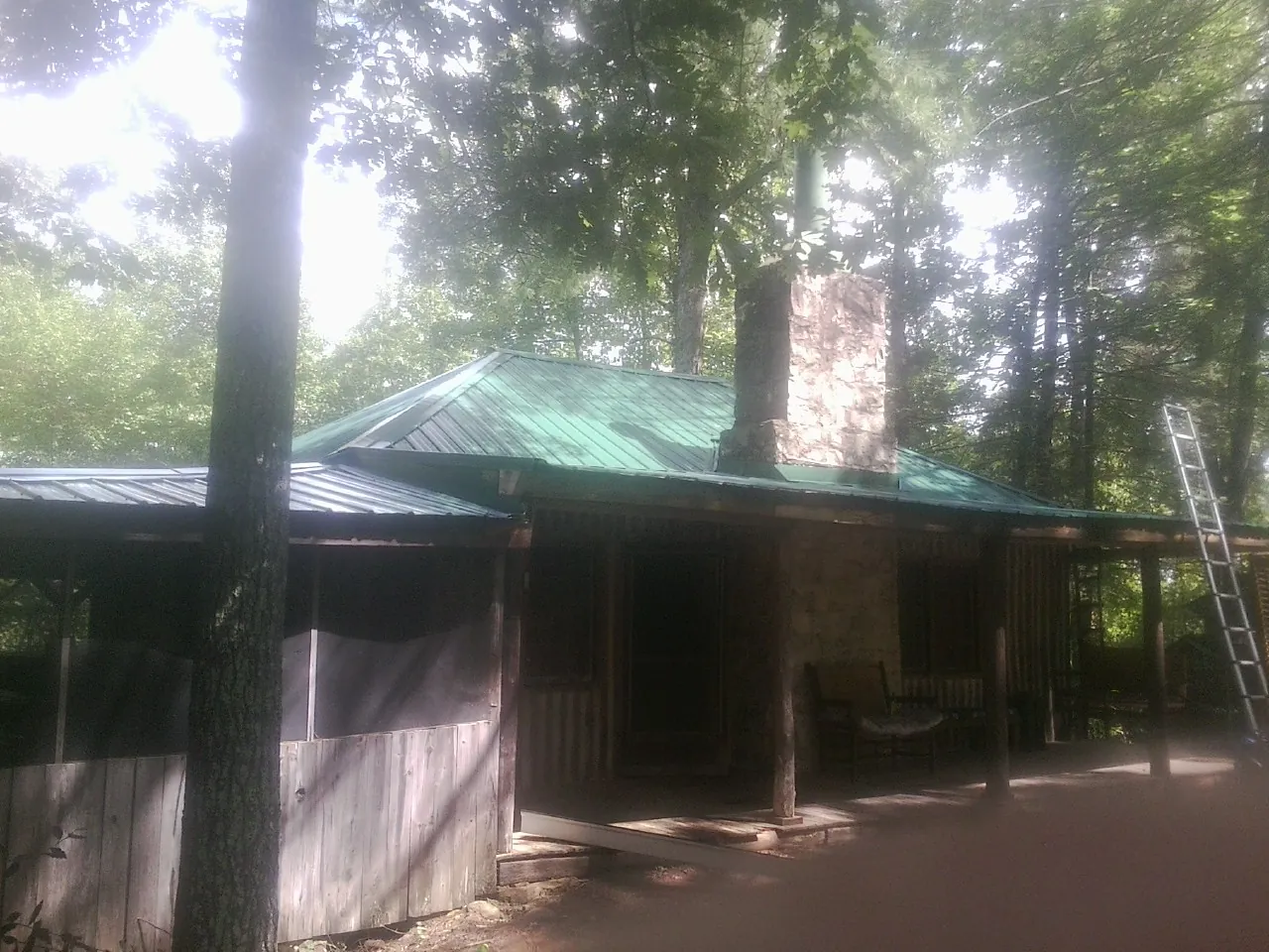 Green metal roof and stone chimney above a log cabin porch in Rossville